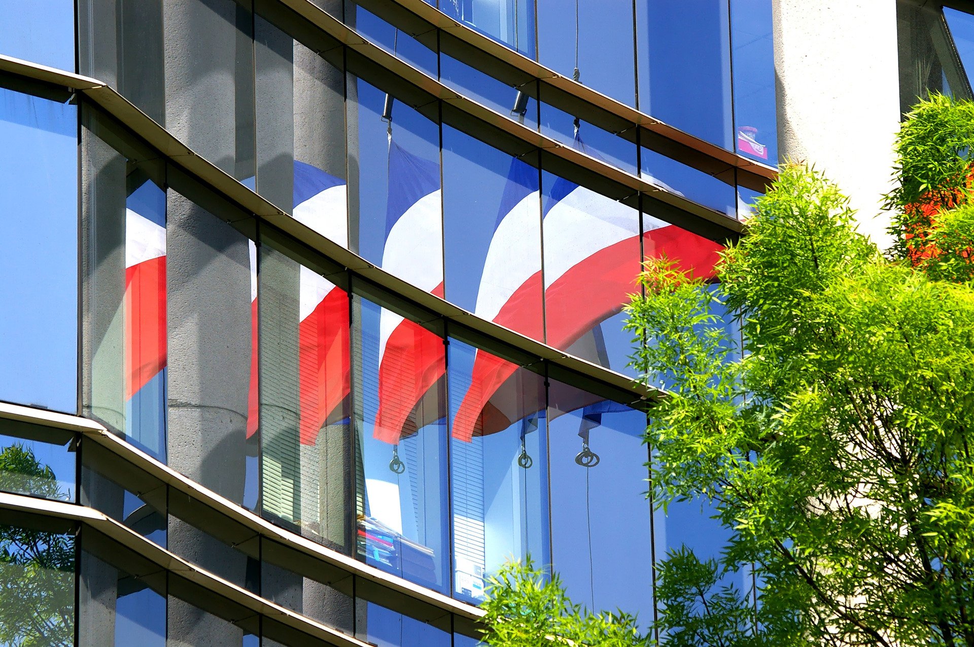 Façade de bâtiment administratif français, le drapeau français est visible en reflet.